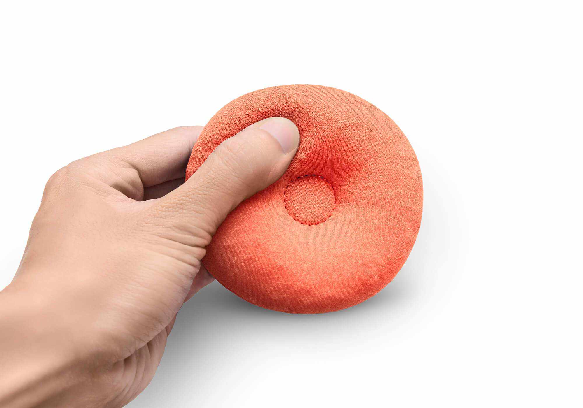 A hand pressing into a soft, round orange fabric eye cup to show its flexible, cushioned texture, isolated on white.