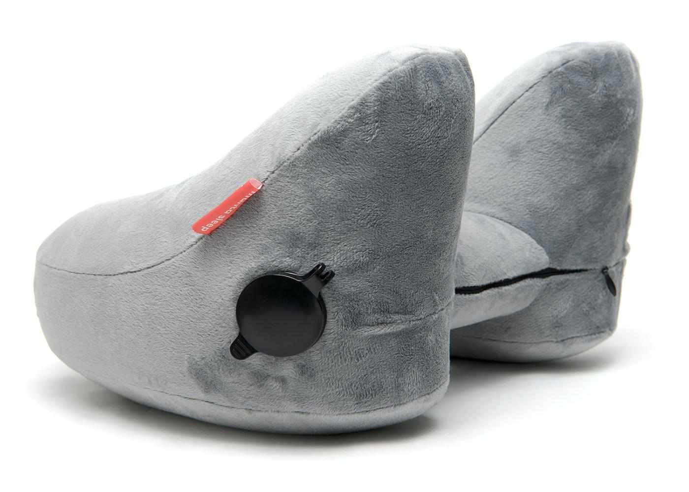 Side angle of a grey plush Manta Travel Pillow showing a black inflation valve and a red Manta Sleep logo tab.