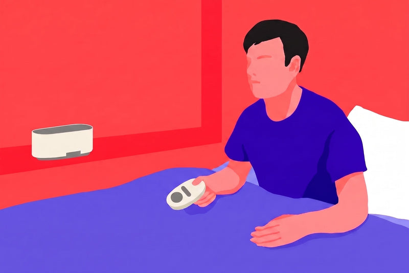 A man sitting on a bed holding the control pad of a white noise machine to operate the speaker on the window sill.