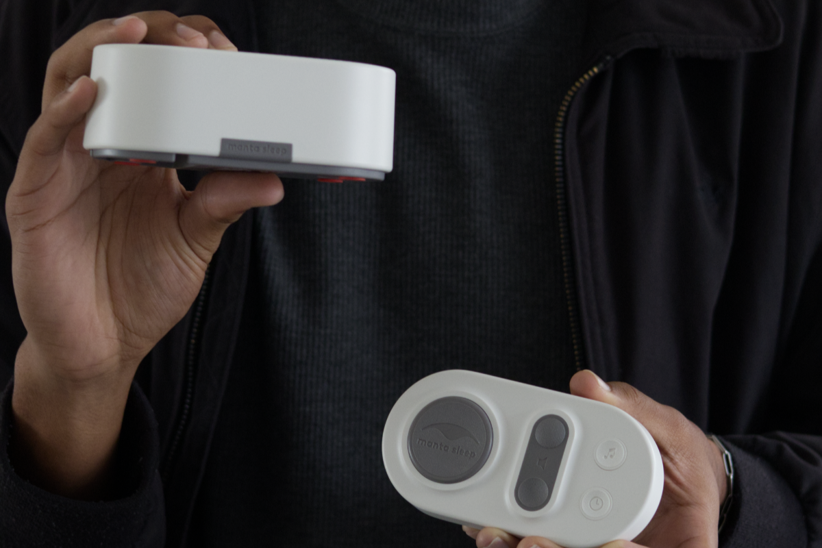 Person holding Manta White Noise Machine in one hand, and its remote in the other hand.