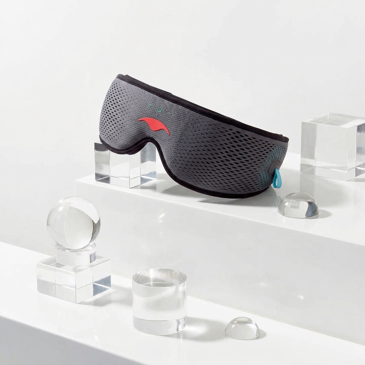 Gray Manta SOUND Sleep Mask on a white surface with transparent glasses and geometric shapes.