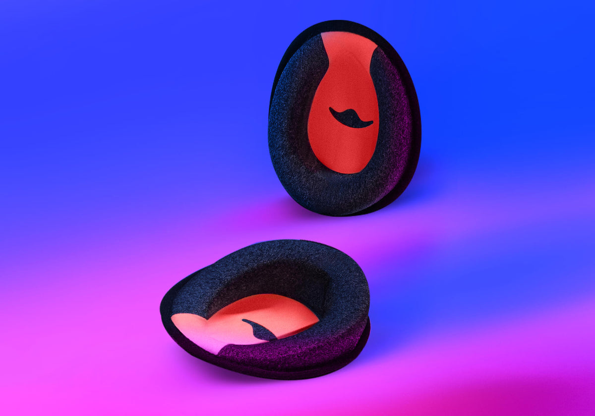 Studio shot showing two C-shaped grey foam eye cups with a red interior, presented from both a front and a side profile view on a blue and pink background.