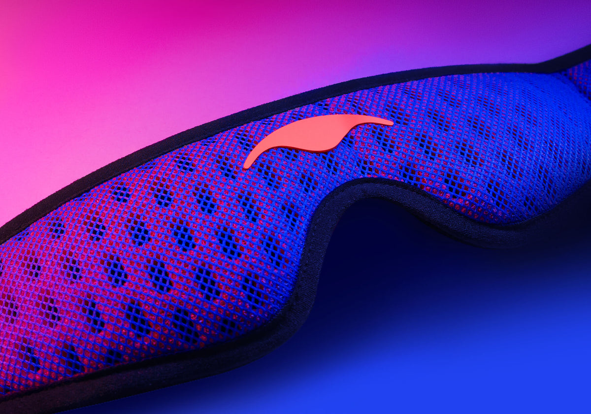 Blue and red Manta PRO Sleep Mask  with a coral-red Manta Sleep Logo laying flat on a gradient pink and blue background.