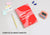 Flat lay of the red Manta Sleep Journal with a pencil, earplugs, stickers, and a digital timer on a plain grey surface.