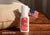 Manta Sleep Pillow Spray bottle standing on a wooden surface by a beige pillow with a small American flag. Text reads: Made in the USA.