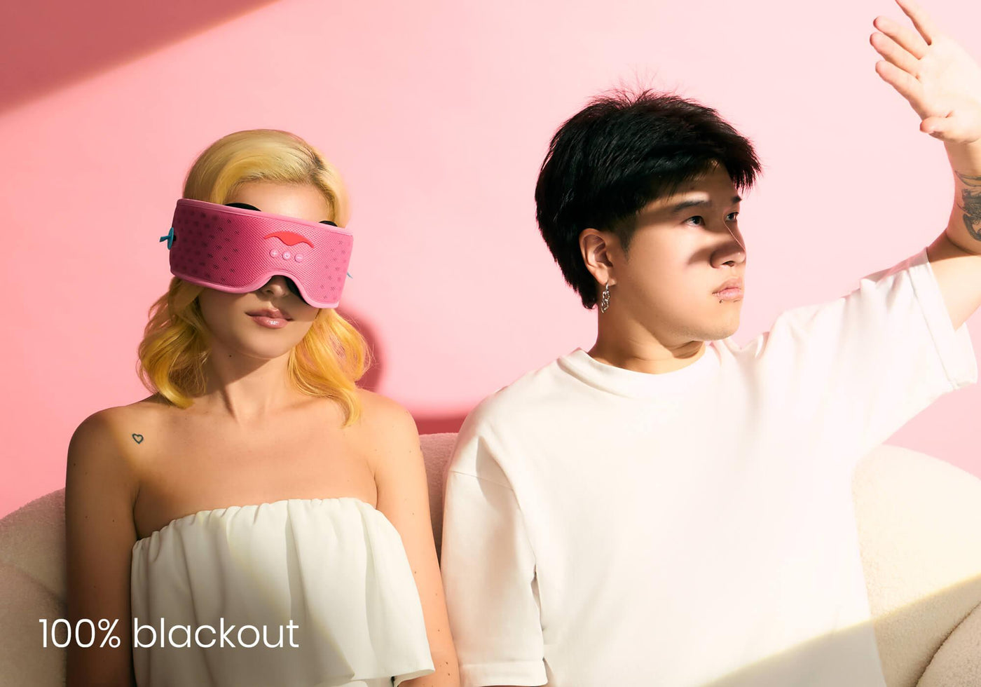 Two people posing, one wears a pink sleep mask, the other shields eyes from light, with '100% blackout' text.