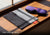 An unfolded grey and black mesh Manta Travel & Laundry Bag resting on a wooden window sill next to a blue and red Manta PRO Sleep Mask in the sunlight. Text overlay: "Fast-drying fabric".