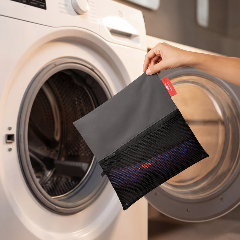 Person holding a black and gray Manta Travel & Laundry Bag in front of a washing machine.