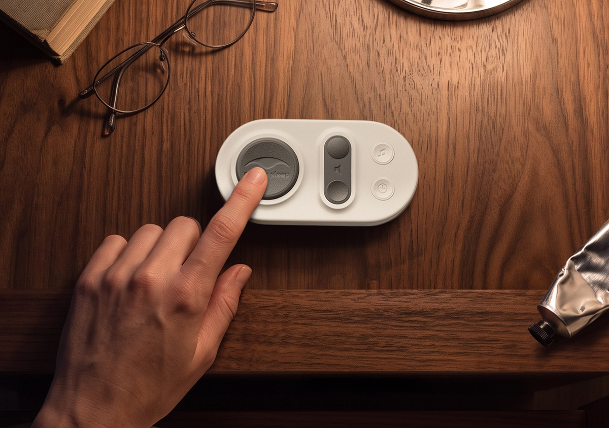 A hand pressing a button on a Manta White Noise Machine remote pad, placed on a wooden desk next to eyeglasses and other desk items.