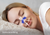 Close-up of a smiling woman sleeping on a plush pillow with a blue nasal strip on her nose and airflow graphics. Text overlay: "Eases breathing".