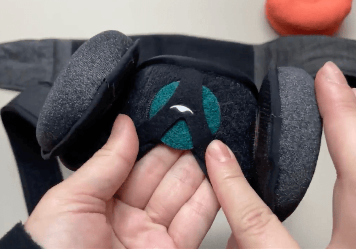 Close-up of a person's hands holding a Manta Sleep Mask with Eucalyptus Manta AROMA Dot attached to it.
