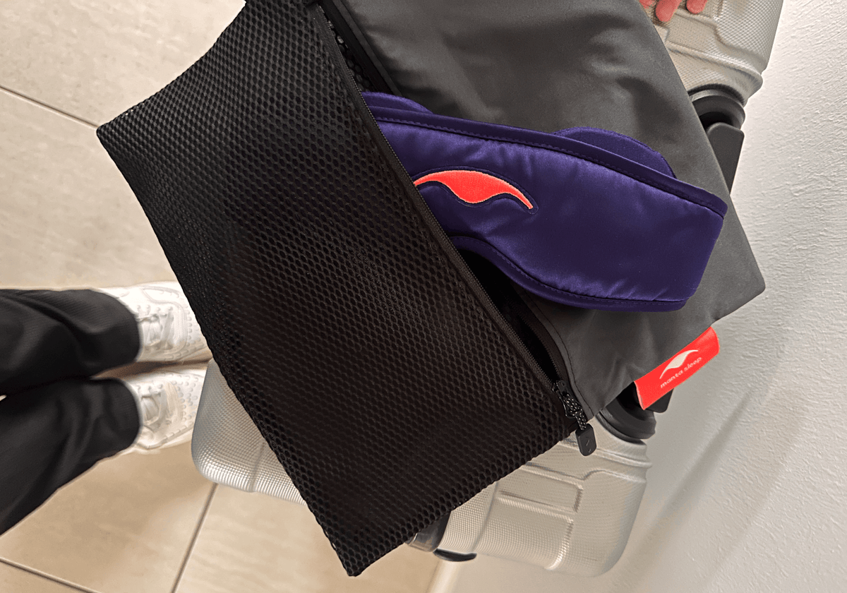 A close-up of a Manta Travel & Laundry Bag containing a purple Manta SILK Sleep Mask logo, placed on top of a silver suitcase.